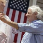 Smiling senior couple dancing with an American flag background, celebrating Independence Day.