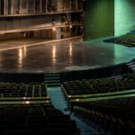 Wide-angle view of an empty theater auditorium with rows of seats facing a grand stage.