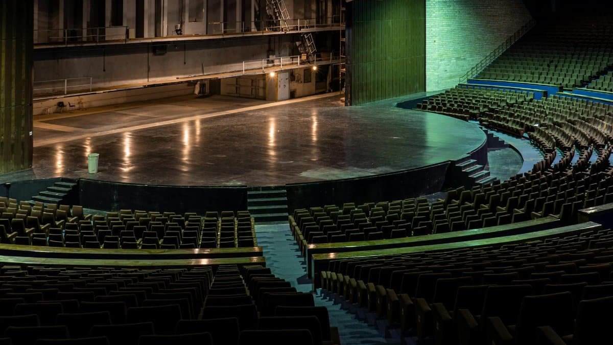Wide-angle view of an empty theater auditorium with rows of seats facing a grand stage.
