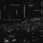 Black and white photo of a large audience in an auditorium with a speaker at the lectern in Oradea.