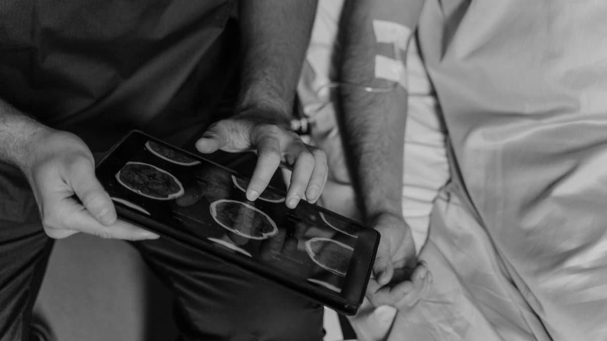 Medical professional reviews patient's CT scans on a digital tablet in grayscale.