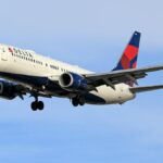 Delta Airlines aircraft soaring in clear blue sky, showcasing aviation travel.