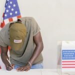 Man casting vote at polling station with American flag in background.