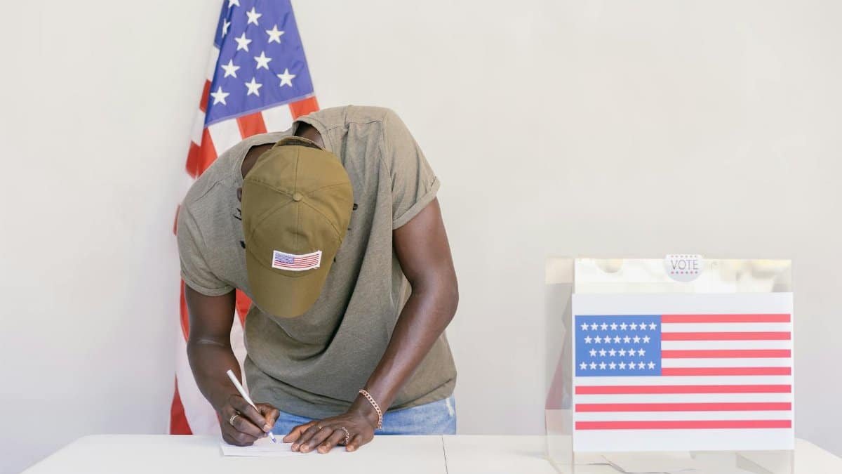 Man casting vote at polling station with American flag in background.