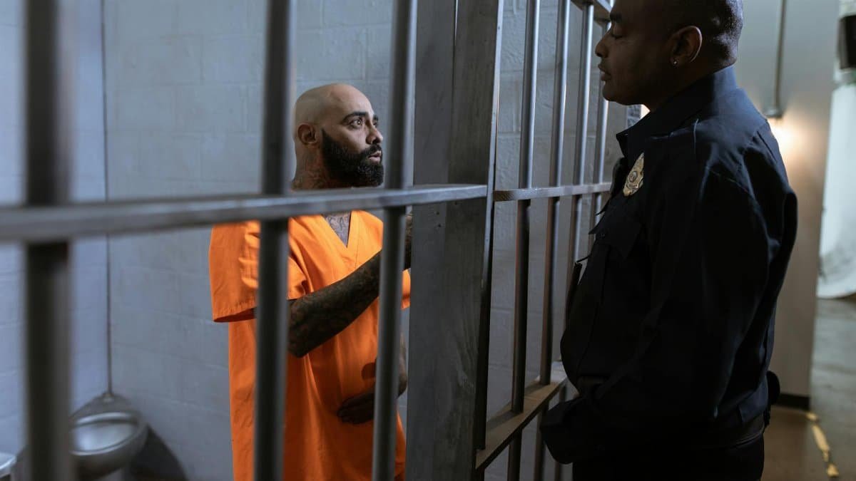 A guard converses with an inmate inside a prison cell, highlighting the justice system setting.