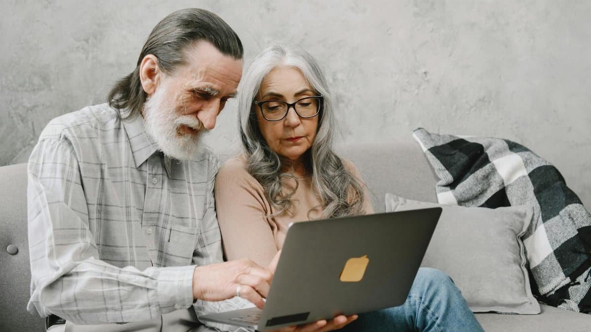 Elderly couple sitting on a couch using a laptop, sharing a moment of togetherness.