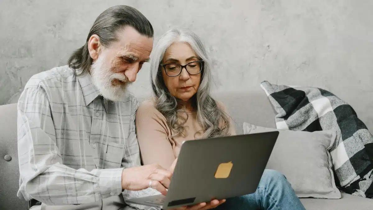 Elderly couple sitting on a couch using a laptop, sharing a moment of togetherness.