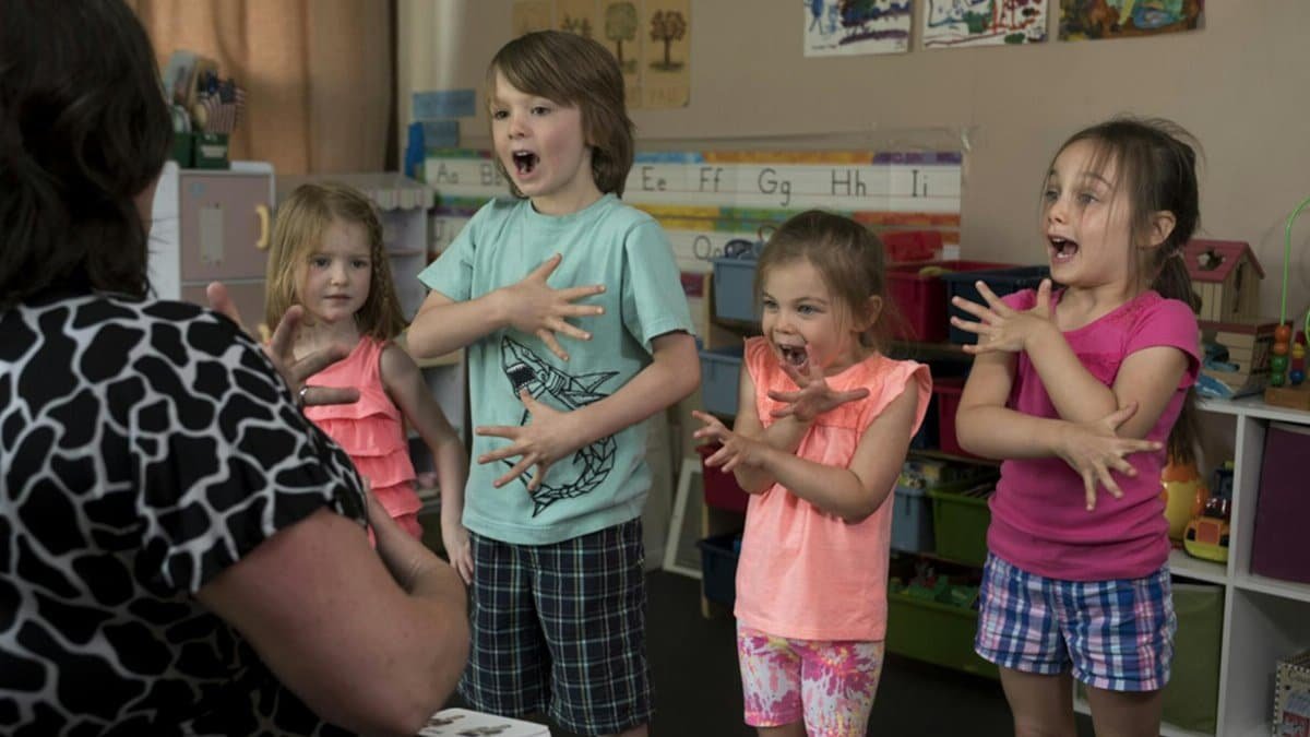 Children learning sign language with a teacher in a vibrant classroom setting.