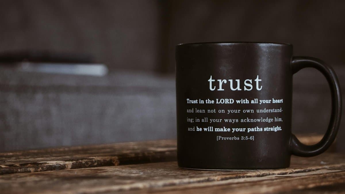 Black ceramic mug with white religious text from Holy Bible placed on shabby wooden surface in room
