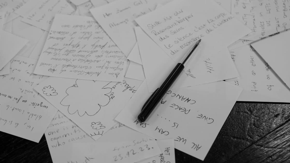 A collection of handwritten notes scattered on a desk with a pen in black and white.