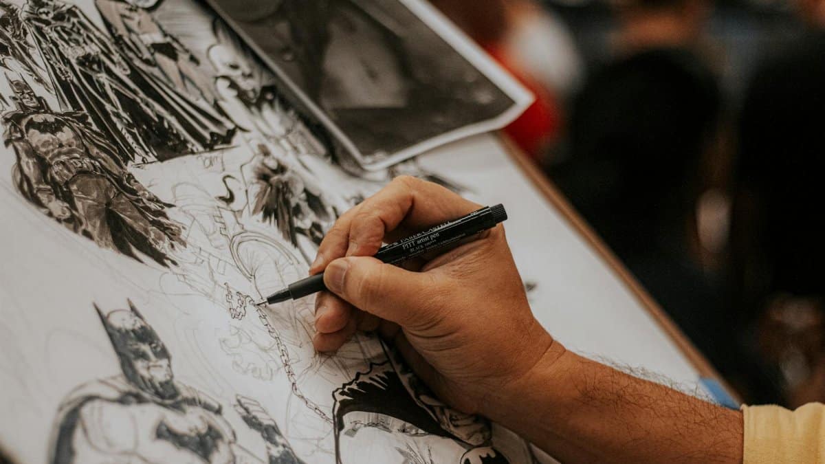 Artist drawing detailed comic book characters with a pen at a lively event.