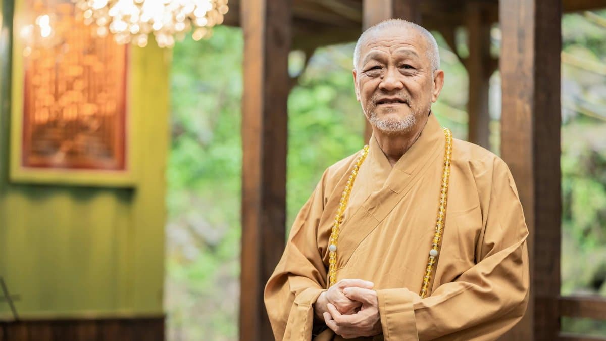 Elderly Buddhist monk standing indoors in traditional garments. Spiritual and peaceful setting.