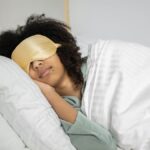 A woman with afro hair sleeps soundly in bed with a sleep mask, enjoying a cozy indoor atmosphere.