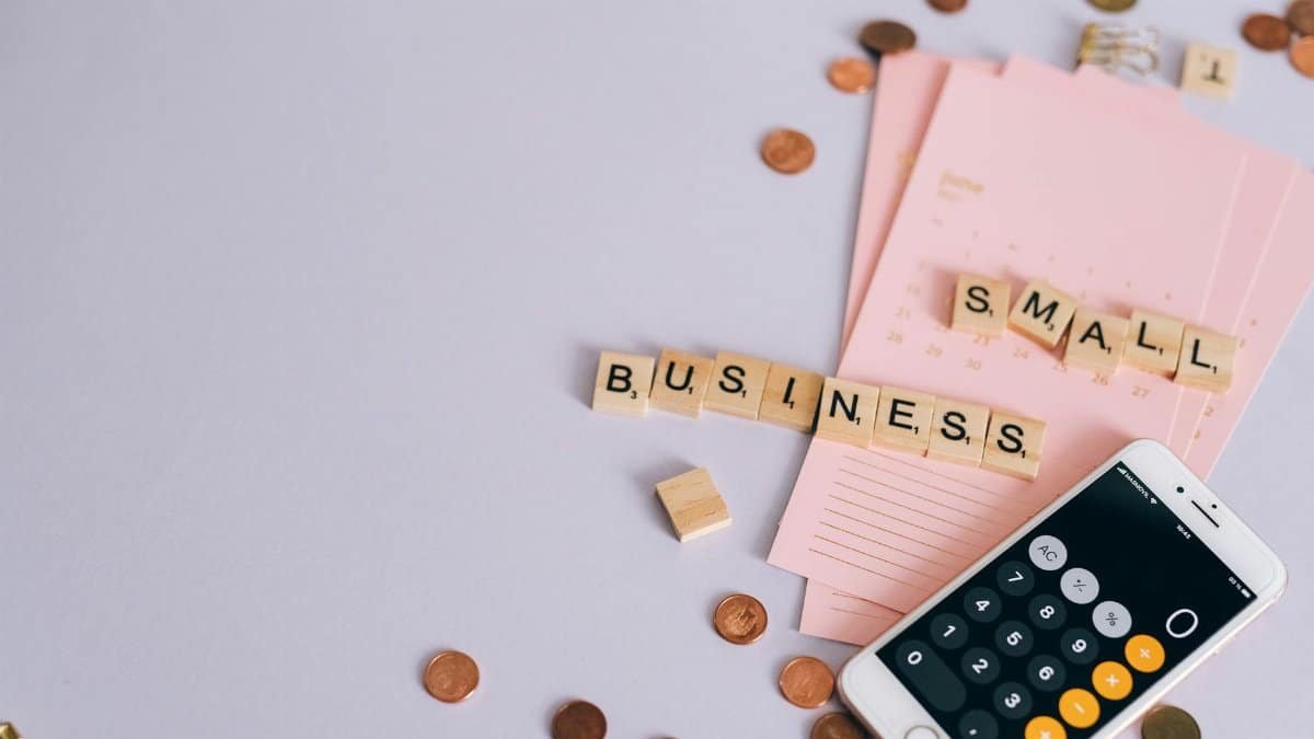 Flat lay of a small business planning scene with coins, smartphone calculator, and letter tiles.