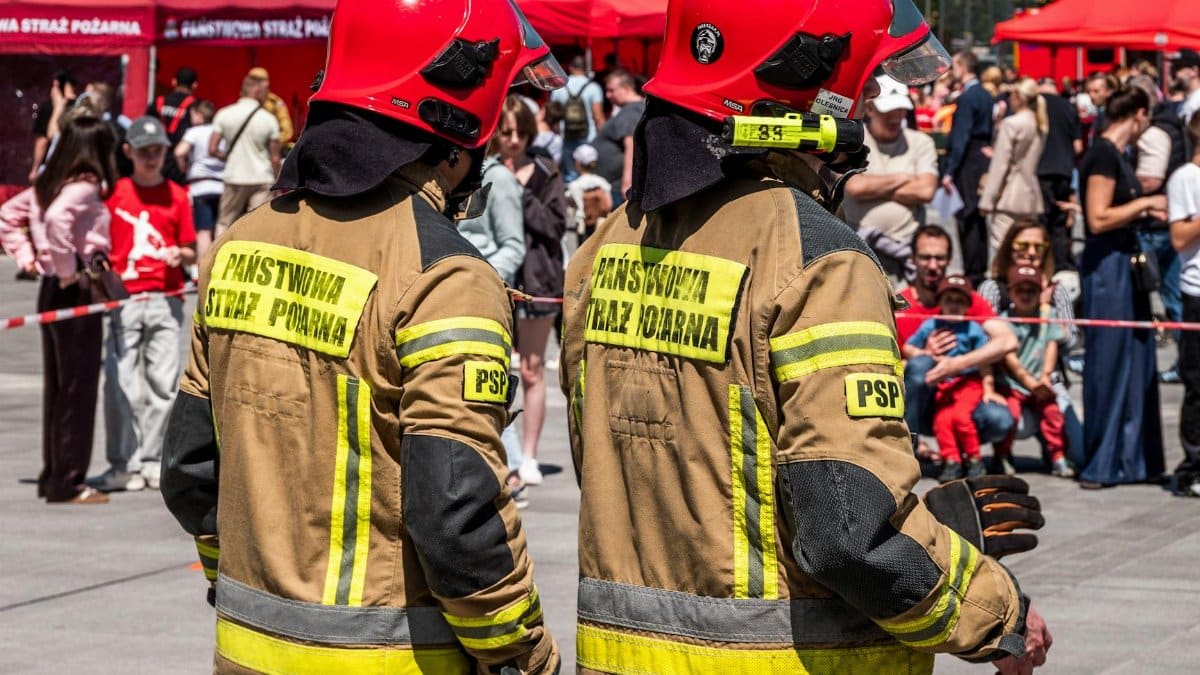 Two Polish firefighters in red helmets at a public safety event outdoors.