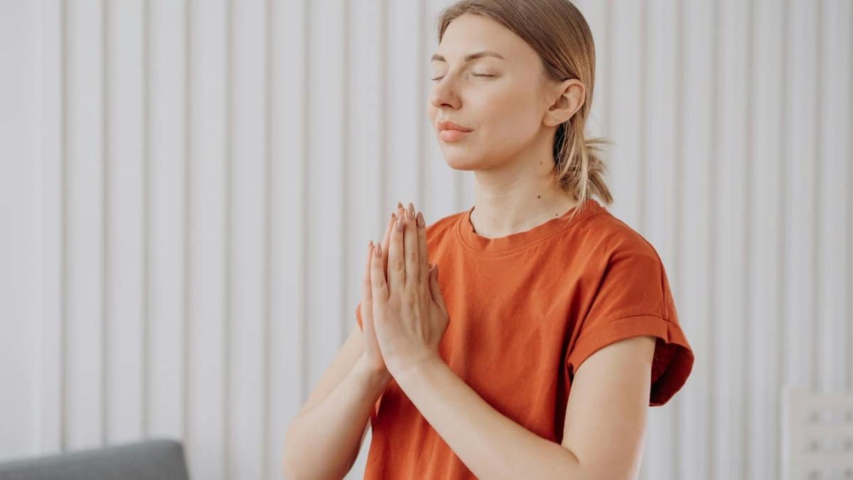 A woman in orange practices meditation indoors, expressing mindfulness and concentration.