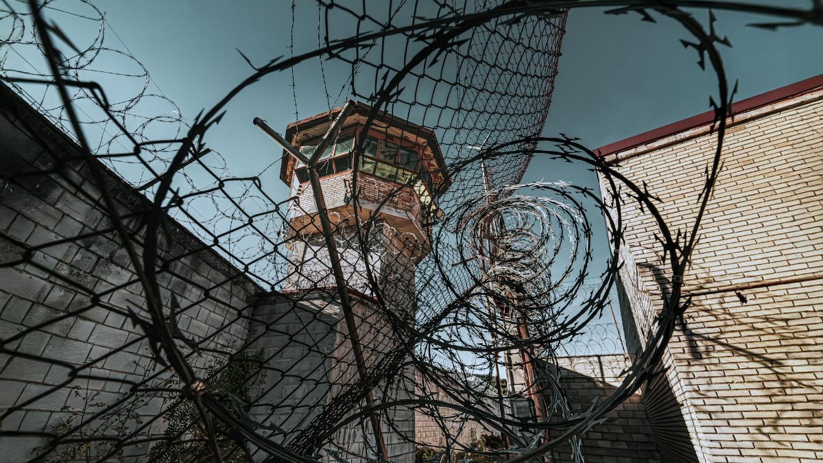 Dramatic view of a guard tower through barbed wire in a prison yard, symbolizing security and confinement.