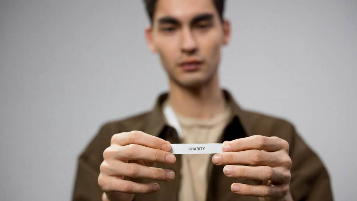 A man holds a note reading 'charity,' with the focus on his hands, expressing a charitable theme.