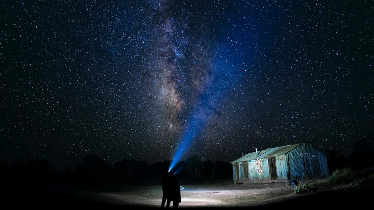 Couple embracing under the Milky Way, highlighted by a rustic barn and starry sky.
