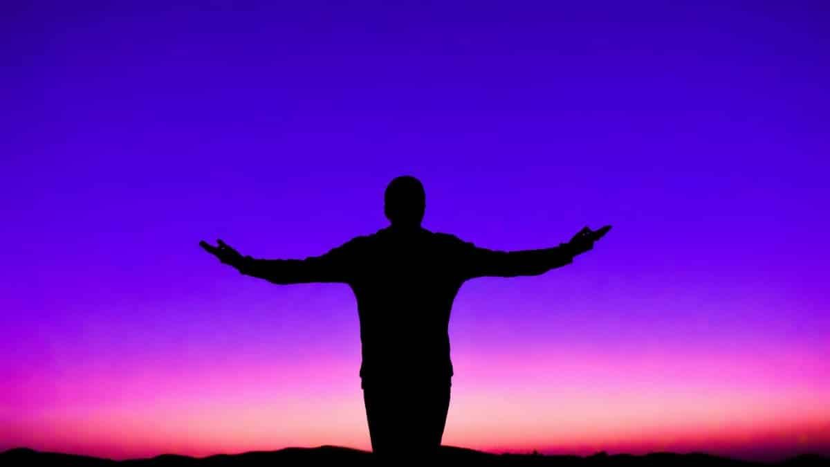 Silhouette of a person with outstretched arms against a vivid sunset sky.