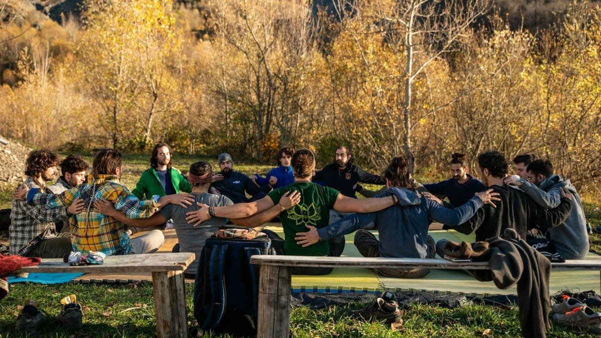 A diverse group sitting in a circle outdoors, embracing in an autumn setting.