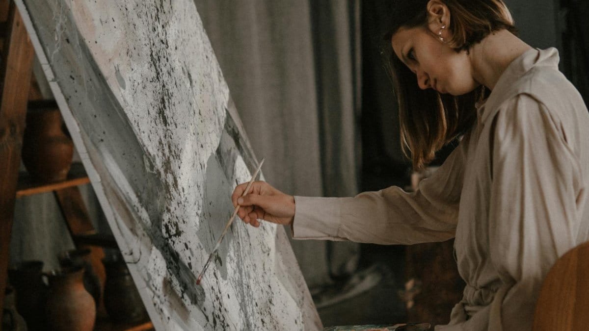 A young woman concentrates while painting on a large canvas in her art studio.