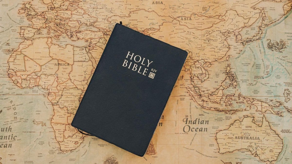 Holy Bible resting on an old-fashioned world map. Inspirational travel and faith concept.