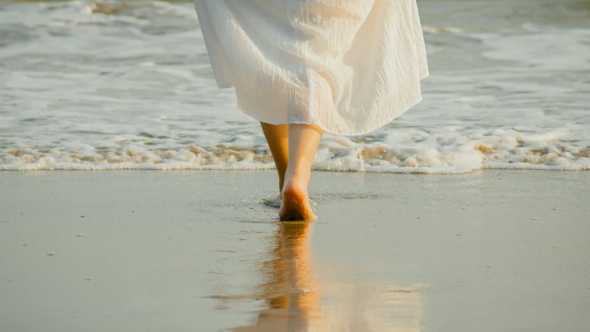 Serene scene of a woman walking along a beach shore at sunset.