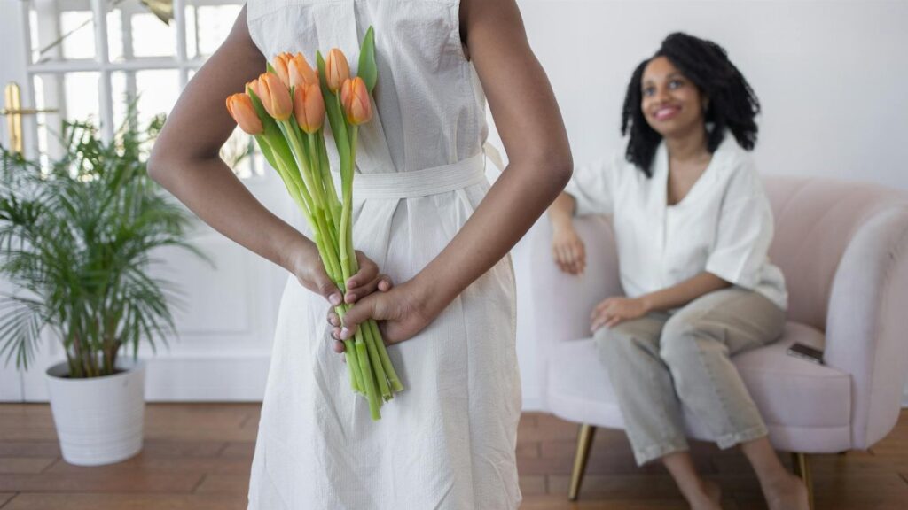 A child surprises their mother with tulips indoors, depicting warmth and love.