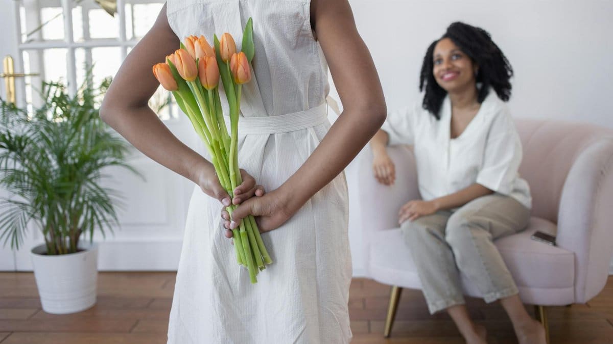 A child surprises their mother with tulips indoors, depicting warmth and love.