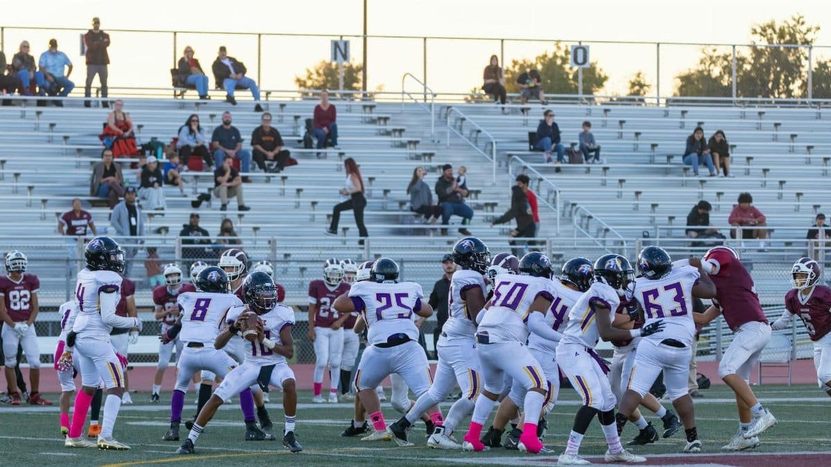 Players compete in a high school American football game with fans in the bleachers.