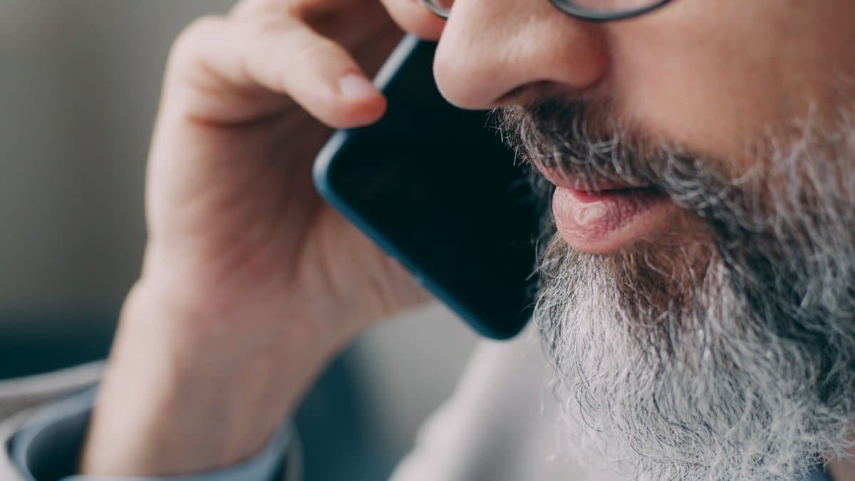 Close-up of a bearded man speaking on the phone indoors.