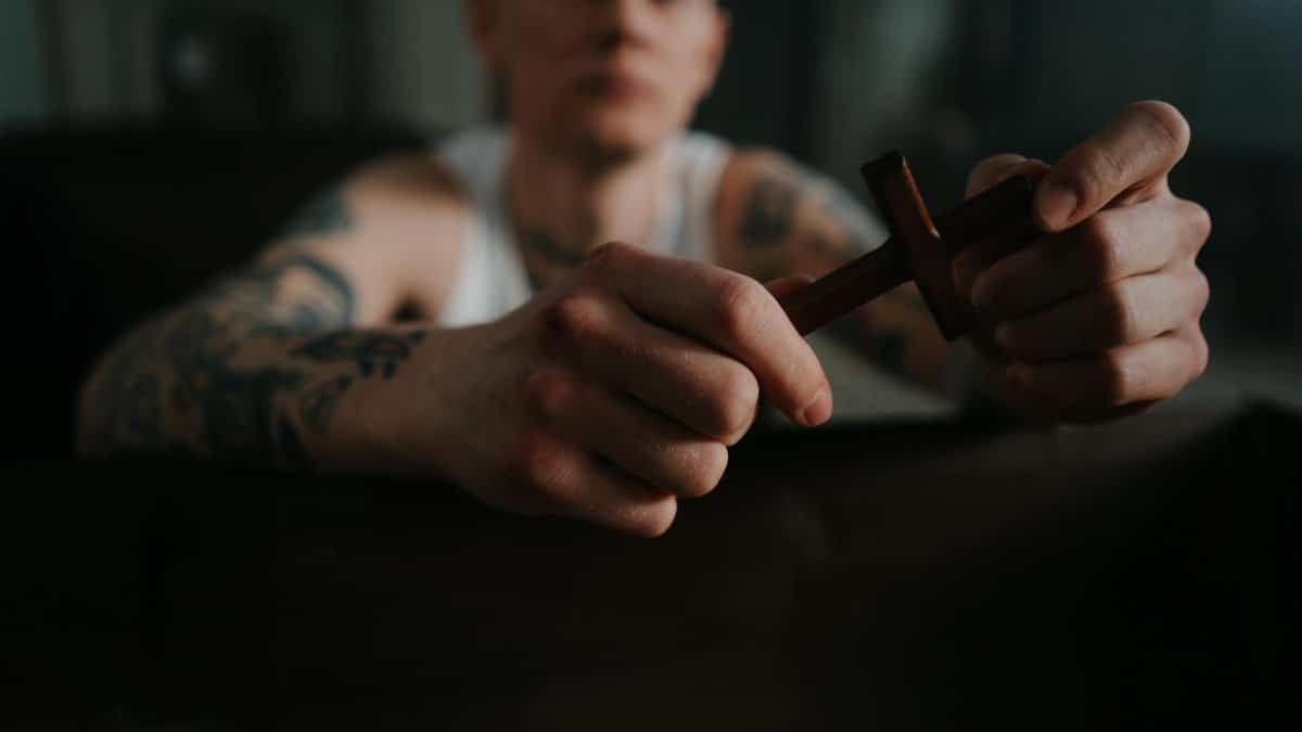 A tattooed man holding a wooden cross, symbolizing faith and contemplation indoors.