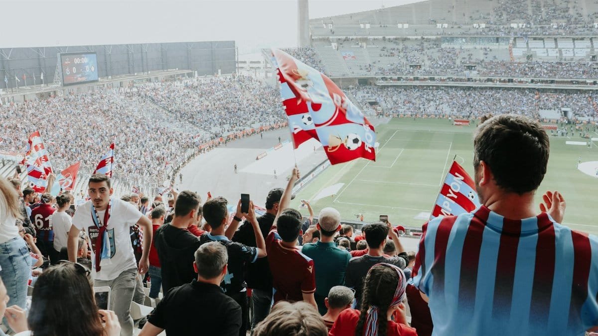Soccer fans waving flags and celebrating victory in a packed stadium.
