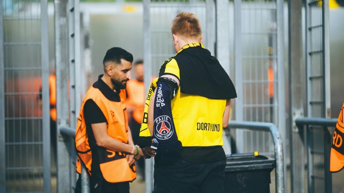 Security personnel and a fan at a football stadium checkpoint in Dortmund, Germany.