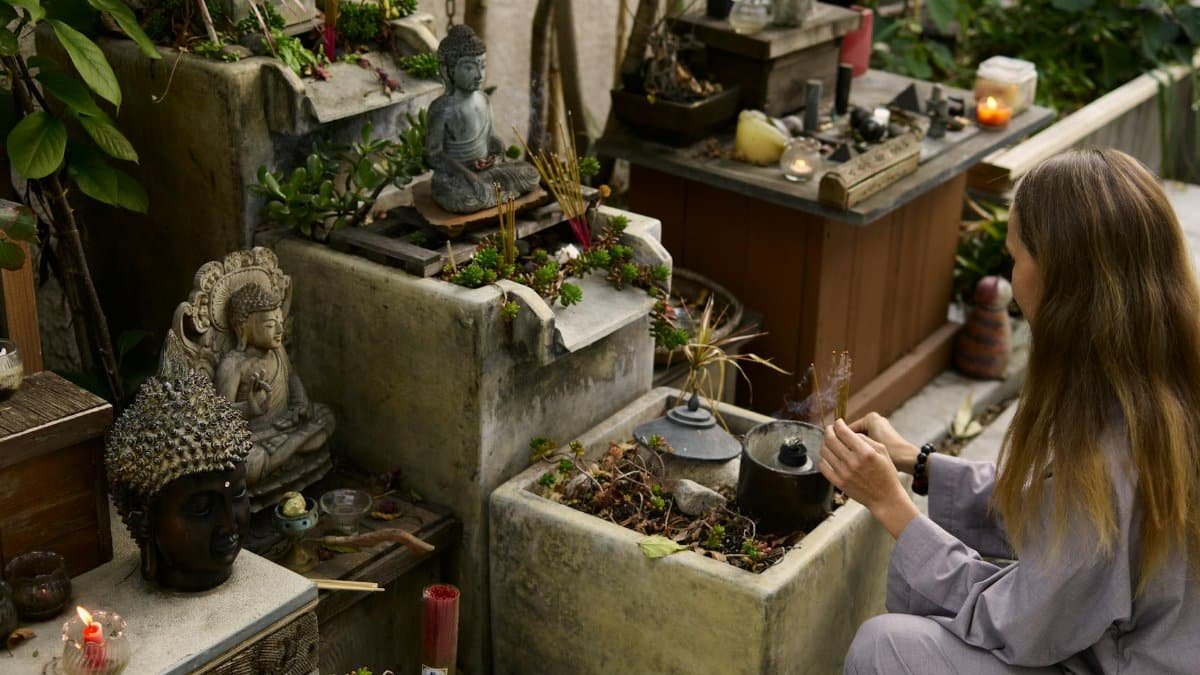 A woman at an outdoor shrine performing a ritual with Buddha statues and incense.