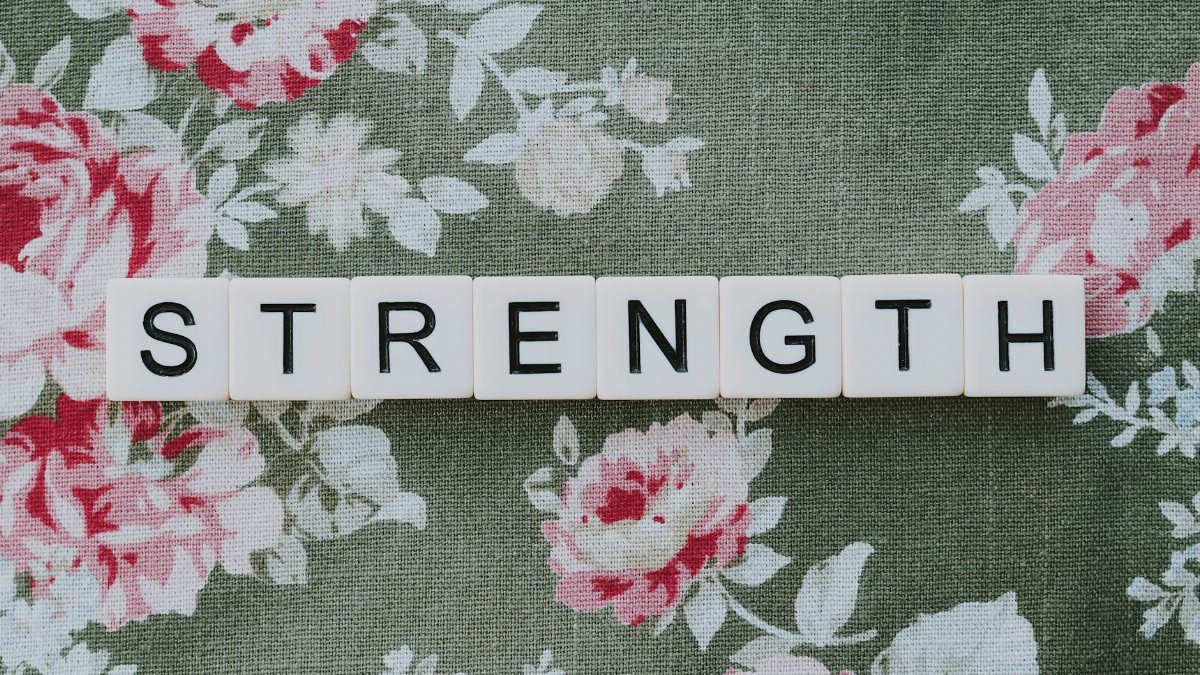 White letter blocks spelling strength on floral textile background.