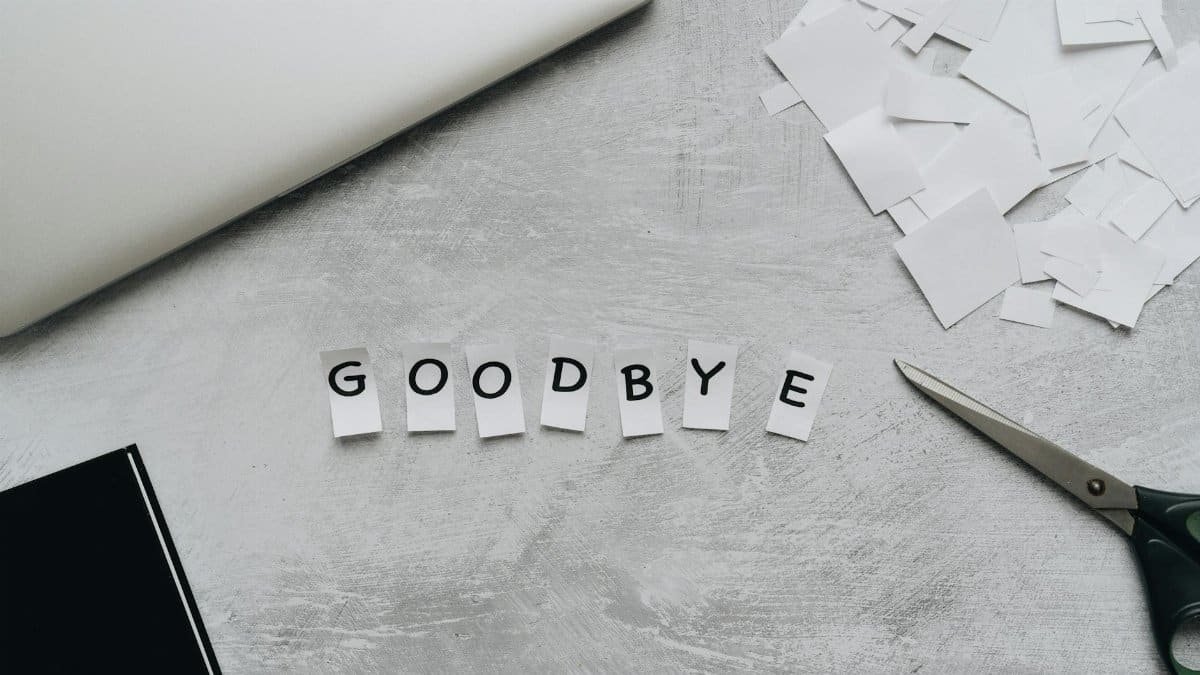 Artistic flat lay featuring the word 'GOODBYE' crafted from paper cutouts with scissors and a laptop.