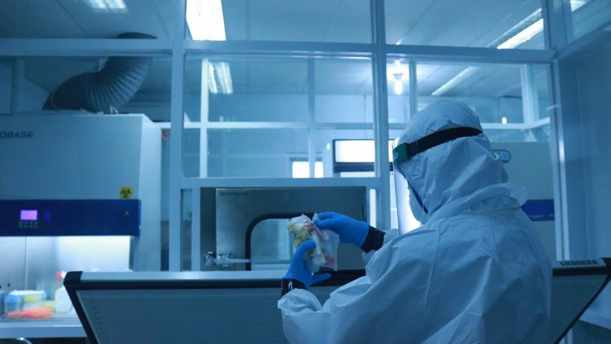 Lab technician in full protective suit performs tasks in a controlled laboratory environment.