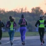Four people running outdoors at dawn, wearing activewear and reflective gear for visibility.