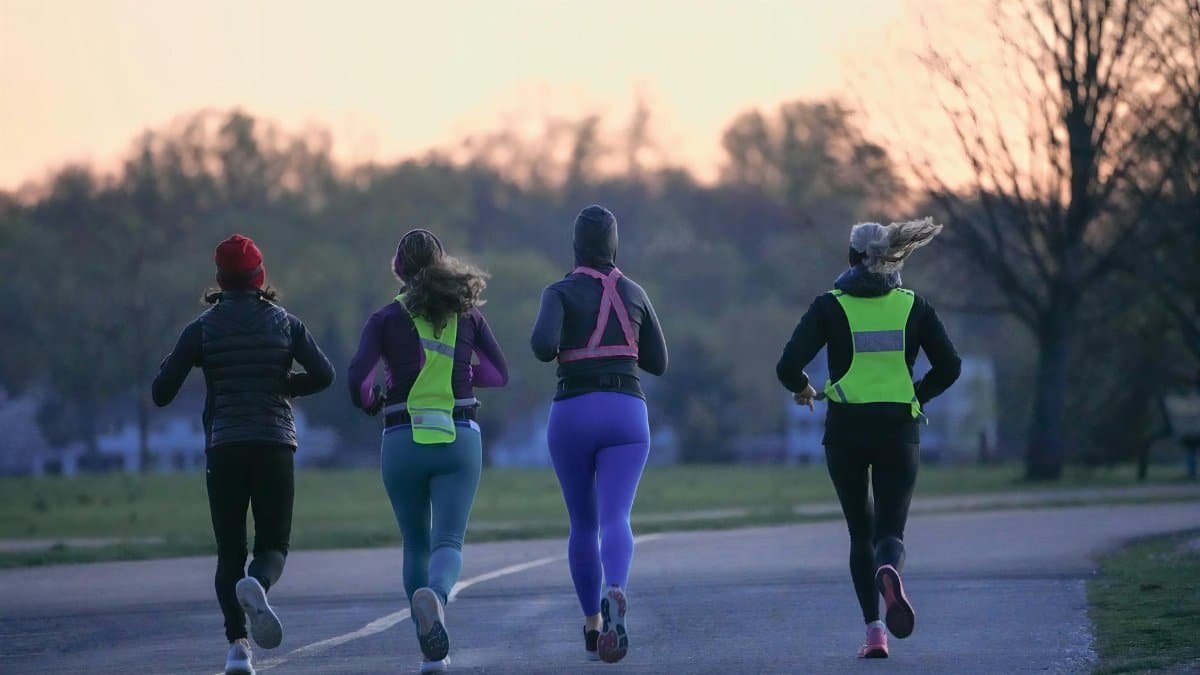 Four people running outdoors at dawn, wearing activewear and reflective gear for visibility.