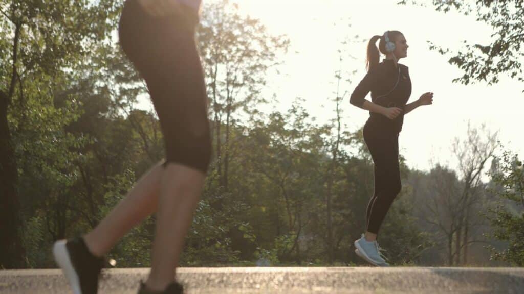 Two women jogging in a sunny park setting, enjoying a healthy morning exercise.