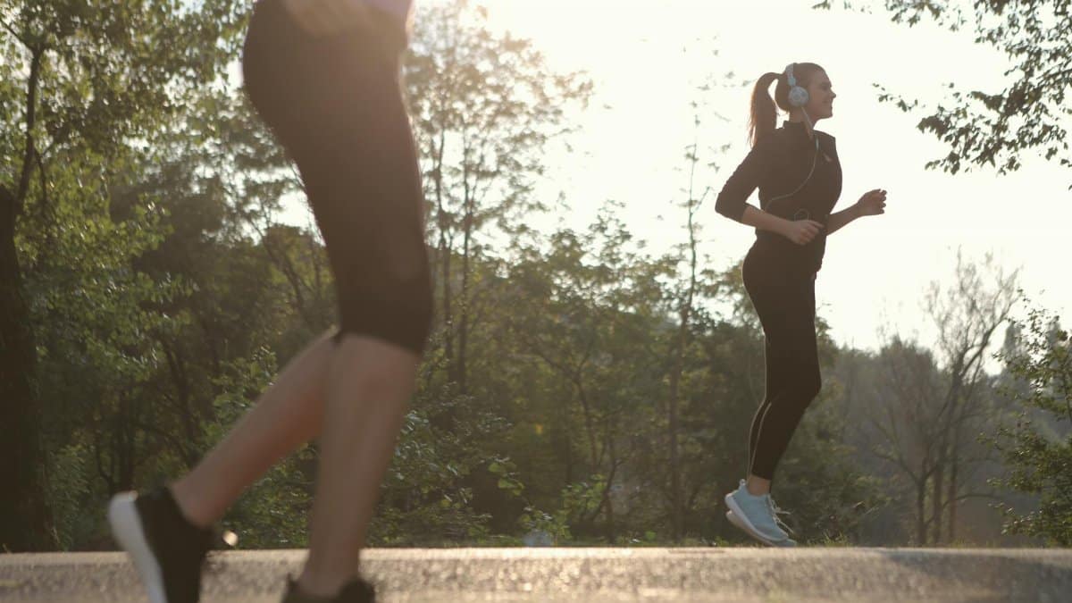 Two women jogging in a sunny park setting, enjoying a healthy morning exercise.