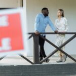 A black man and caucasian woman discussing a property for sale on a porch. Ideal for real estate content.