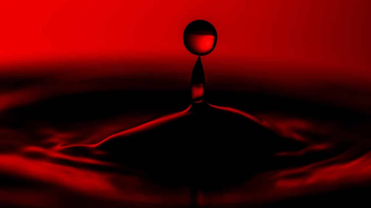 Close-up image capturing the dramatic splash of a water drop on a vivid red background.