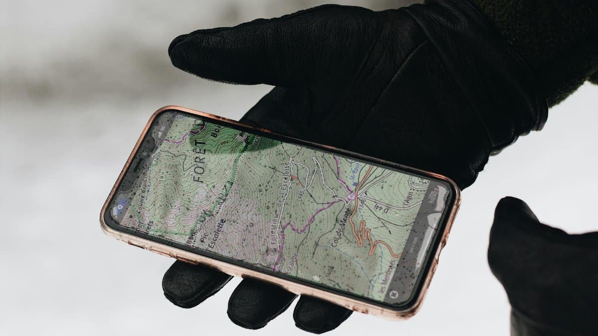 A gloved hand holds a smartphone with a map app displayed, showcasing navigation in cold weather.
