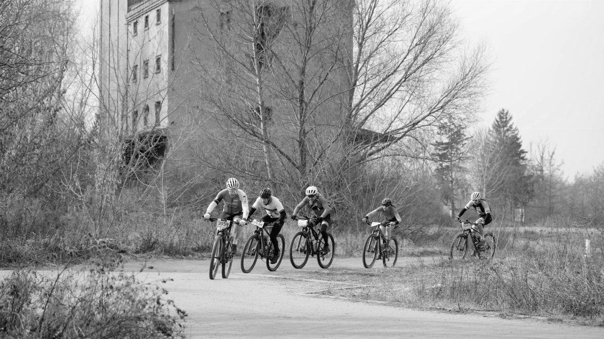 A black and white photo of cyclists racing past an abandoned building, creating a vintage atmosphere.
