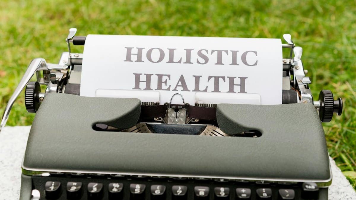 A vintage typewriter in a grassy outdoor setting displaying 'Holistic Health' on paper.