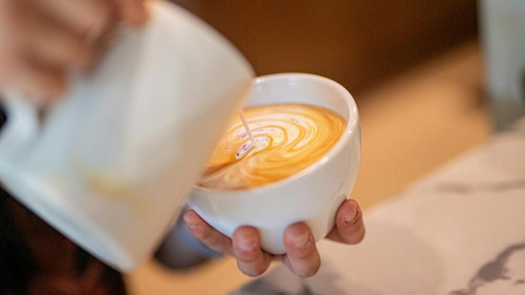 Close-up of a barista pouring latte art in a coffee shop, showcasing skillful design.