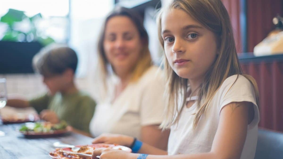 A family enjoying a meal together, focusing on a young girl at the dining table.